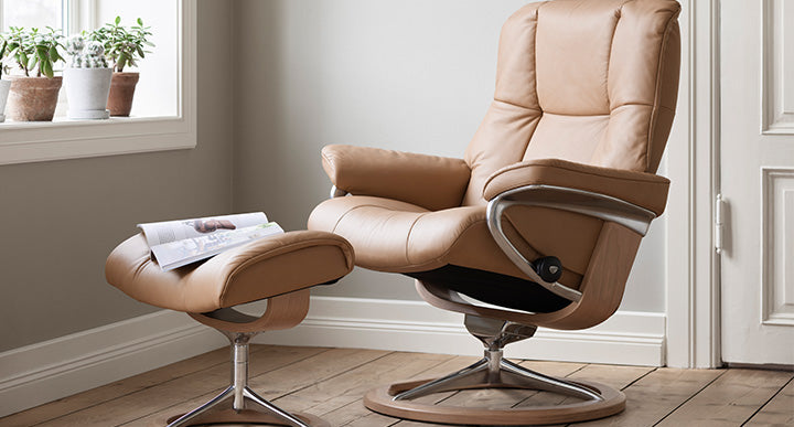 A tan leather recliner with matching footstool in a bright, minimalist room with wooden floors.